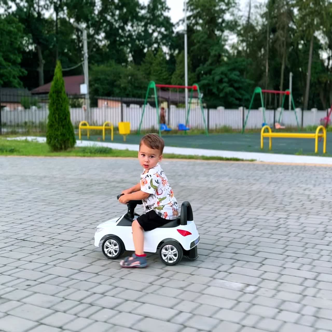 Bambino adorabile e sorridente che guida un'auto giocattolo all'aperto. Bambino felice che trascorre del tempo vicino al parco giochi in estate