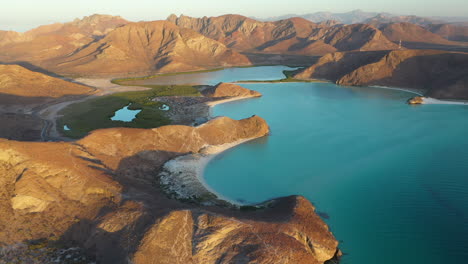 cinematic wide rotating drone shot of balandra beach, view of red hills, turquoise waters, white-sand beaches, and mountains