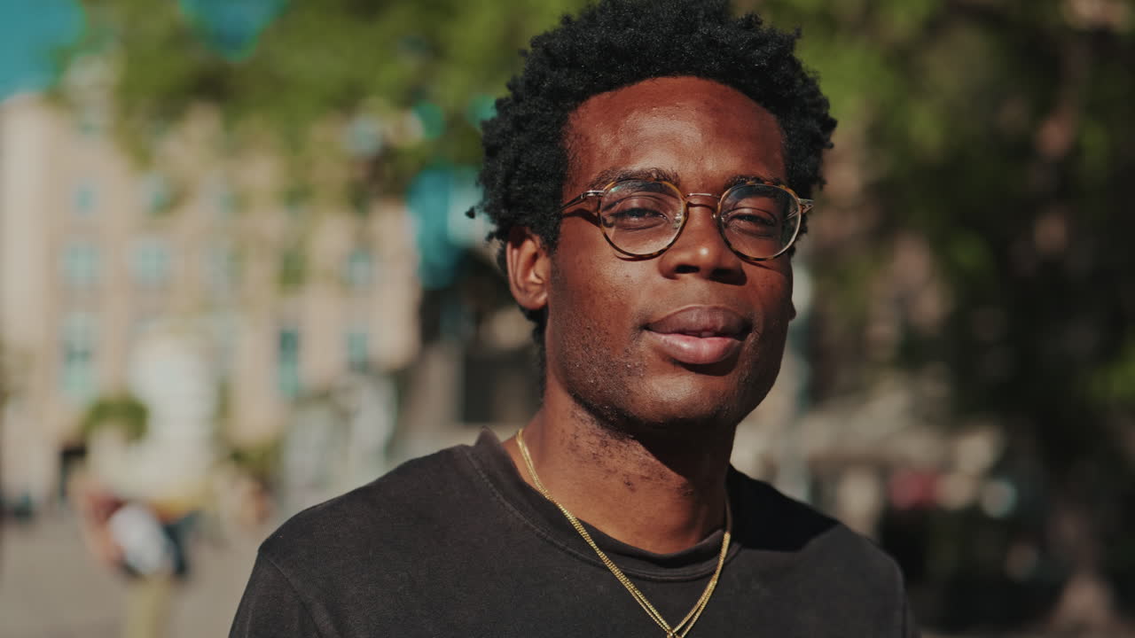 Joven afroamericano con gafas sonriendo a la cámara al aire libre