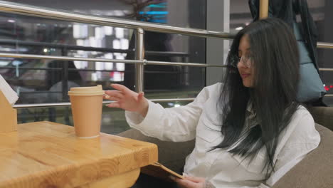 Novelist seated in restaurant with coffee cup on table takes gentle sip before placing it back and continuing to read book in relaxed evening setting with warm lights and thoughtful mood