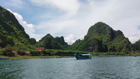 barco vietnamita tradicional navega sobre aguas tranquilas con montaña en segundo plano.
