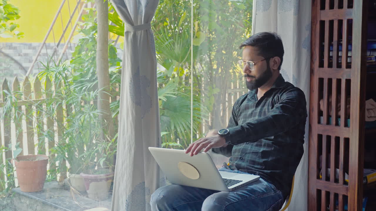indian man saying hello to outsider while working on laptop