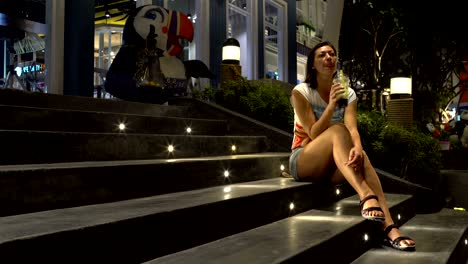 a woman is drinking bubble tea while sitting on the steps of a shopping center