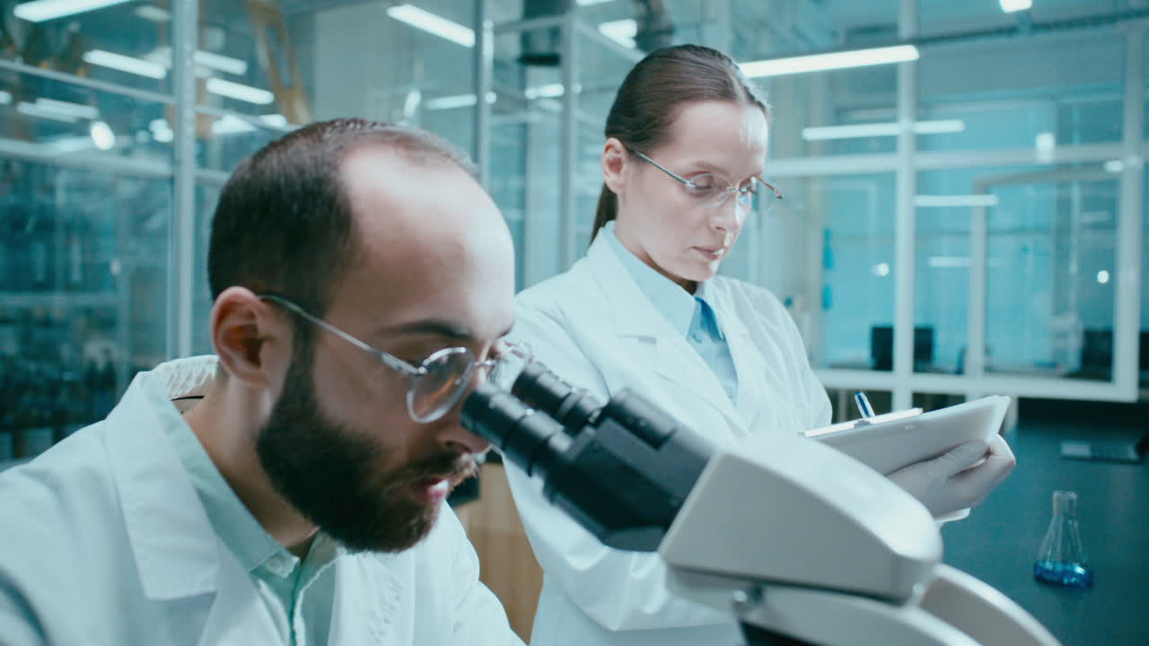 Scienziato uomo che conduce ricerca al microscopio con un collega in laboratorio