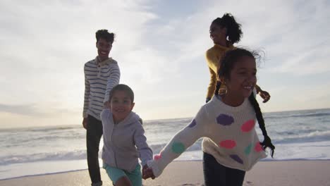 Happy-hispanic-familyholding-hands-and-walking-on-beach-at-sunset