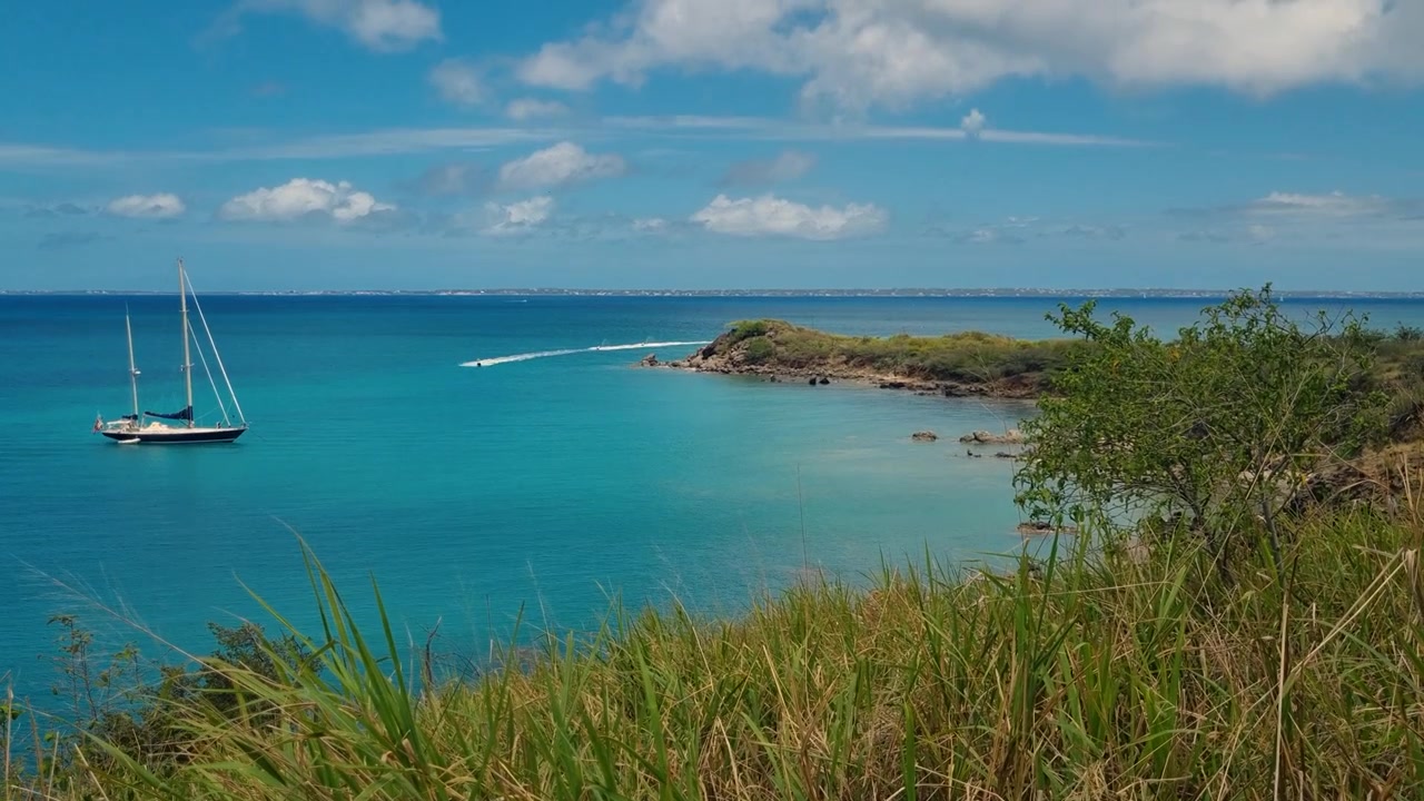 Splendida vista della costa remota vicino a Friars Bay e Happy Bay Beach a St. Martin, che mostra acque caraibiche turchesi, una lussureggiante vegetazione tropicale e una barca a vela solitaria ancorata al largo.