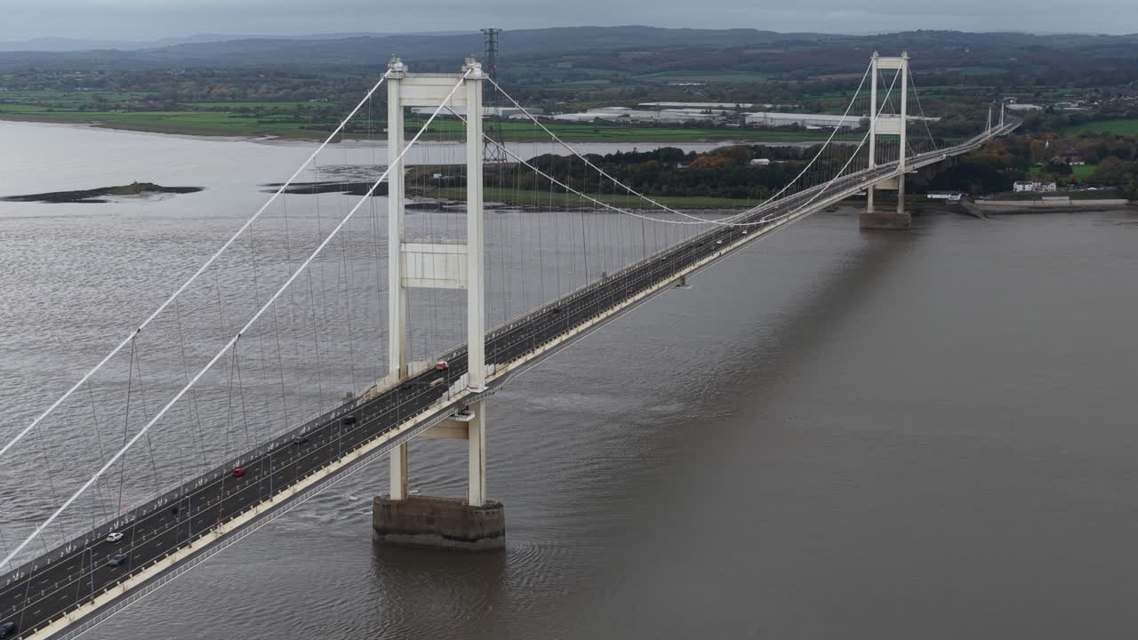 Aerial drone footage of the Severn Bridge spanning the River Severn, showcasing its suspension architecture, vital transportation link between England and Wales, and the surrounding estuary landscape