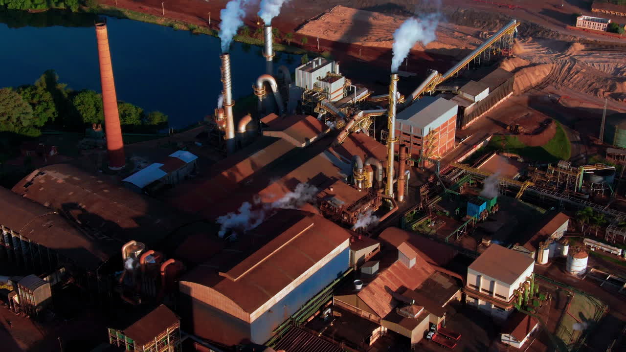 Drone aerial landscape of ethanol production plant warehouse facility factory buildings with steam turbines in countryside rural town by lake and crops Brazil South America industry refinery