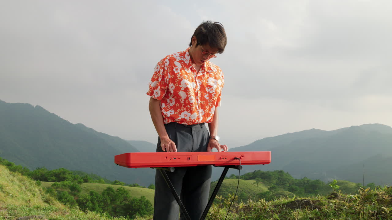 백그라운드에 산이 있는 언덕 꼭대기에서 전자 피아노를 연주하는  ⁇ 스터의 느린 움직임 손  ⁇