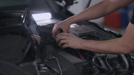 hands mechanic uses a tablet computer with an augmented reality diagnostics software. specialist inspecting the car in order to find broken components inside. male uses laptop for diagnostics vehicle