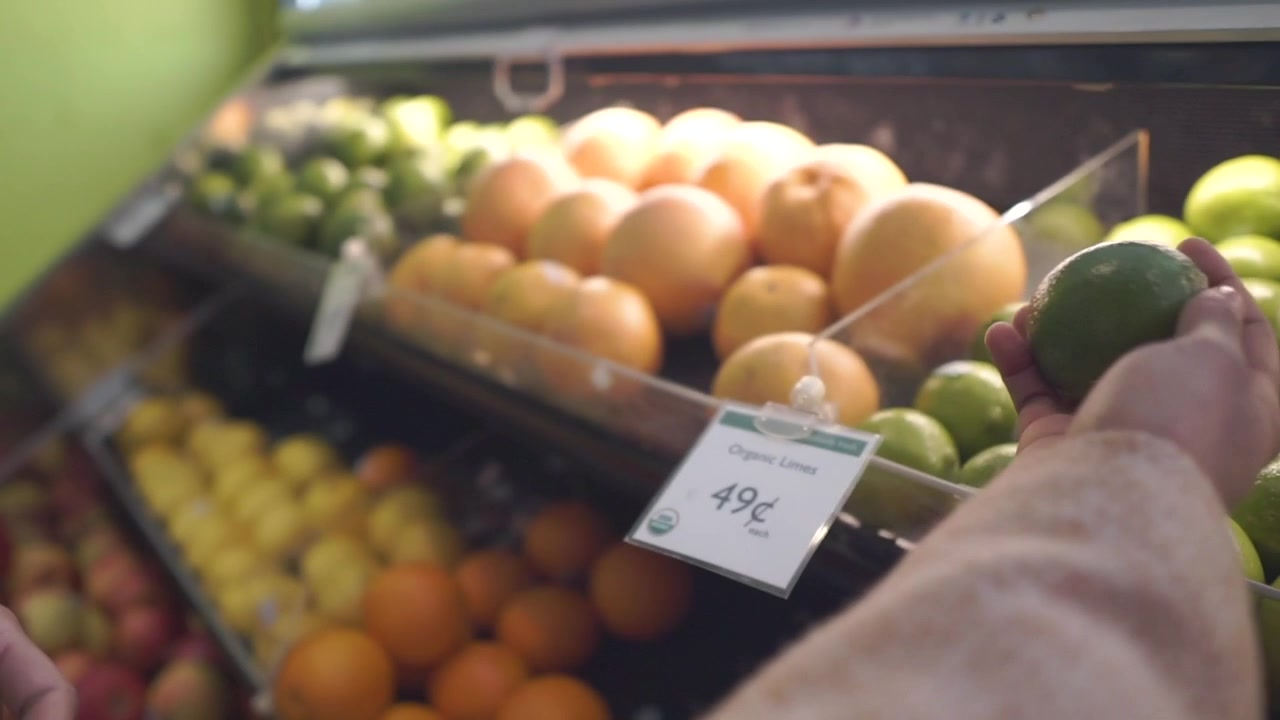 Close-up de uma jovem mulher afro-americana atraente escolhendo limões em um supermercado/feira de frutas e vegetais, com o preço do limão visível.