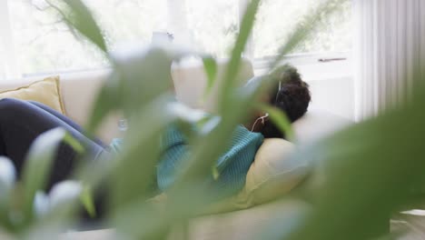 Feliz-Mujer-Afroamericana-Tumbada-En-El-Sofá-Con-Auriculares-Y-Viendo-La-Tableta,-Cámara-Lenta