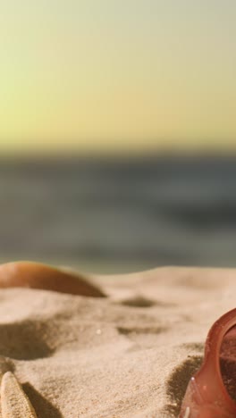 Vertical-Video-Summer-Holiday-Concept-With-Sunglasses-On-Sandy-Beach-Against-Sea-And-Evening-Sky