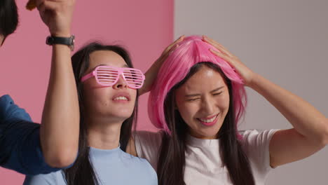 group of young friends in front of pink studio background having fun posing for photo booth style portraits with props 3