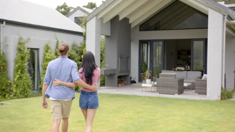 una joven pareja biracial de pie juntos en el patio trasero, mirando a casa, copiar el espacio