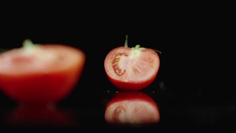 juicy sliced ​​red tomato fall into 2 parts glass with splashes of water in slow motion on a dark background