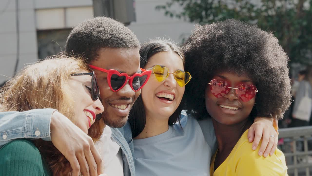 Joyful diverse friends embracing and smiling in heart-shaped sunglasses