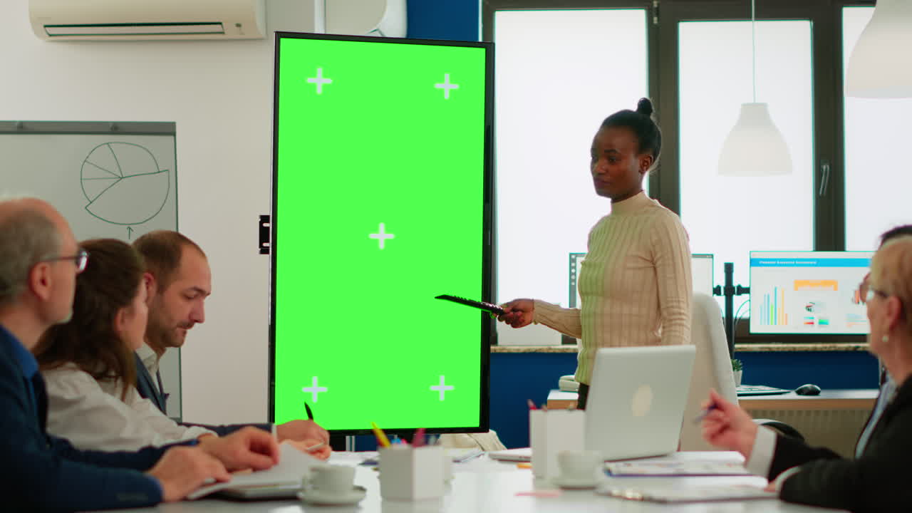 African businesswoman analysing annual reports pointing at green screen monitor