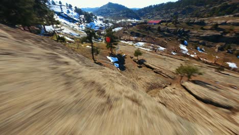 4k fpv drone flying on the side of the mountain, snow and dirt on the ground with trees