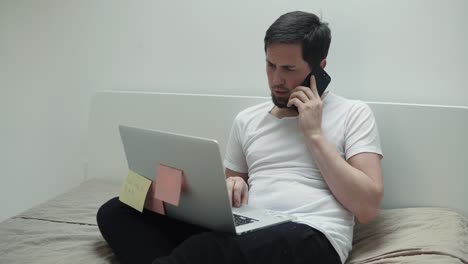 hombre trabajando desde casa en una computadora portátil mientras habla por teléfono