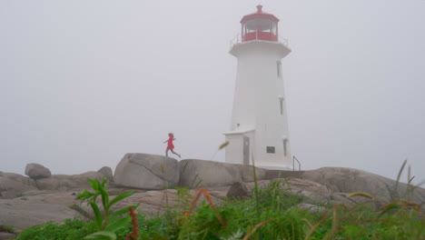 mujer joven caminando hacia el faro en la niebla en un día nublado en nueva escocia, canadá peggy cove