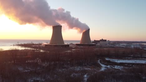 pull back aerial drone shot of nuclear power plant cooling towers at sunrise sunset with steam and smoke winter