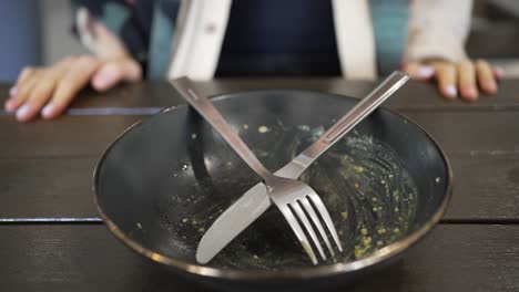 woman puts cutlery in dirty plate after meal in cafe