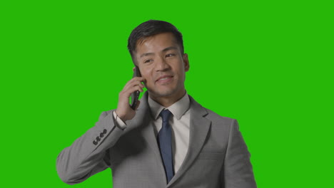 Foto-De-Estudio-De-Un-Hombre-De-Negocios-Sonriente-Con-Traje-Hablando-Por-Teléfono-Móvil-Contra-Una-Pantalla-Verde