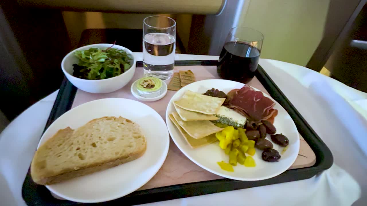 Hand uses fork to eat cheese, olives, and cured meat on airplane meal tray