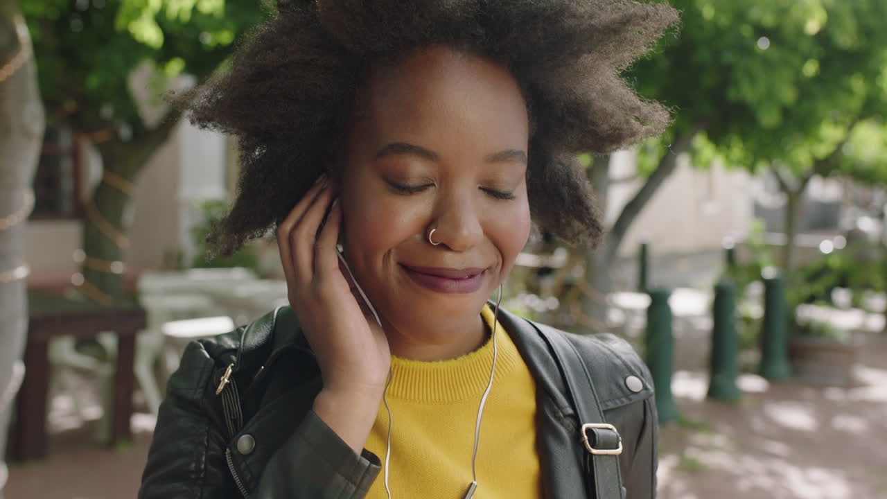 ritratto di una studentessa afroamericana alla moda con un afro funky che sorride allegra godendosi l'ascolto di musica indossando auricolari