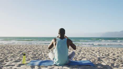 african american man practicing yoga on beach, exercising outdoors by the sea