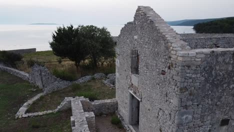 antigua granja abandonada edificio de piedra con pared construida en el lado del mar con ovejas y árbol