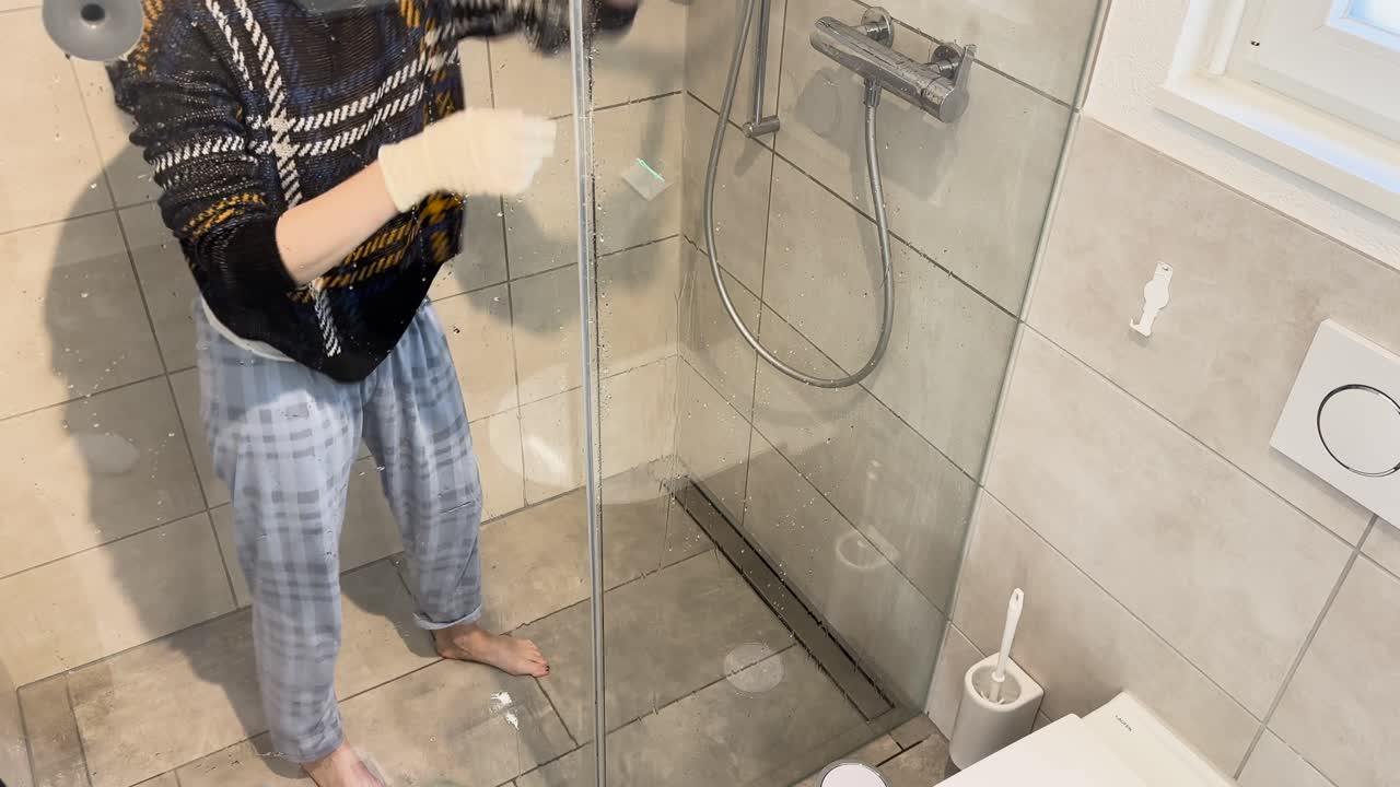 Ovenfra ses en kvinde, der renser et bruserens afløb og skrubber brusergulvet, hvilket viser badeværelseshygiejne, afløbsvedligeholdelse og en realistisk husholdningsrengøringsrutine i et moderne hjem.
