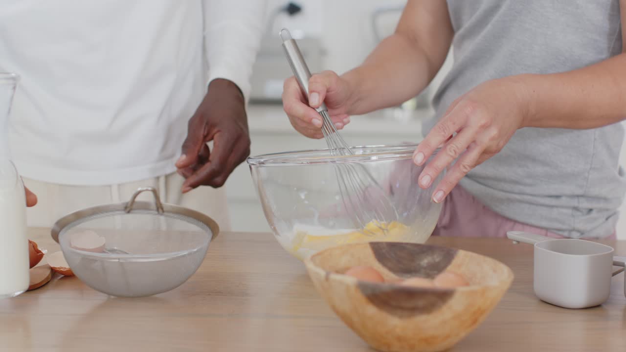 Dopo aver rotto le uova, coppia che versa e sbatte la pastella sul bancone della cucina con frusta e setaccio.