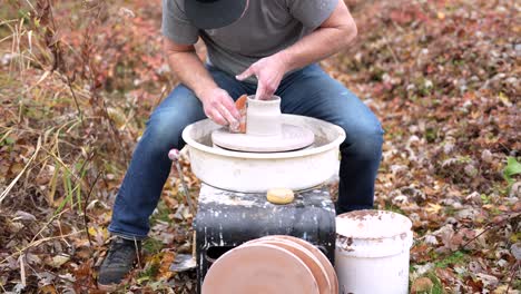 man is using his pottery wheel outside to throw a mug