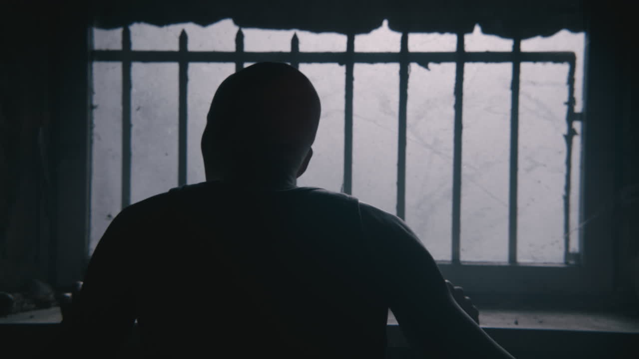 Pale bald skinny man looks through the window in the creepy old bathroom at night