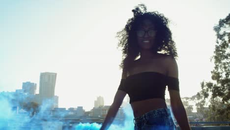 una mujer joven bailando afuera con una granada de humo al atardecer en el garaje del techo