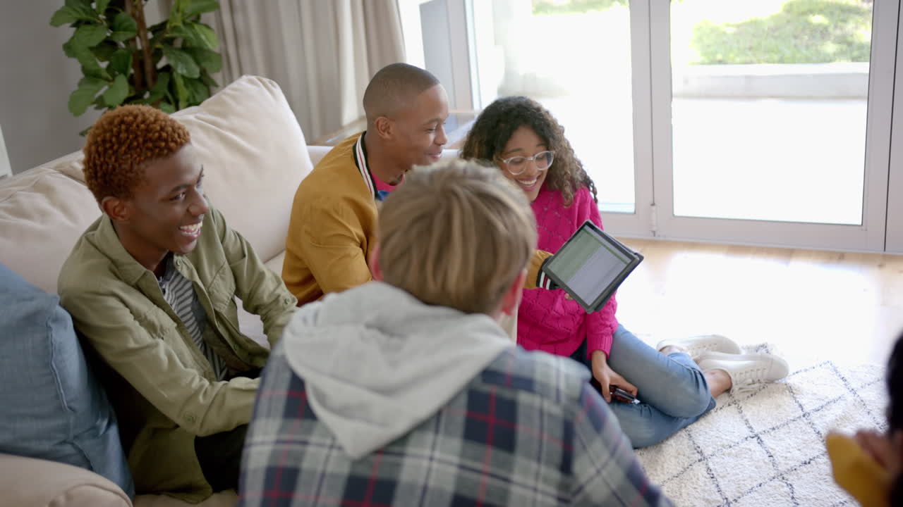Happy diverse group of teenage friends using tablet and talking at home, slow motion