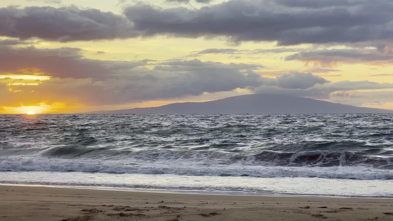 Cinematic wide shot of the sun setting over the horizon next to the private island of Lanai off the coast of Wailea Beach in South Maui, Hawai'i