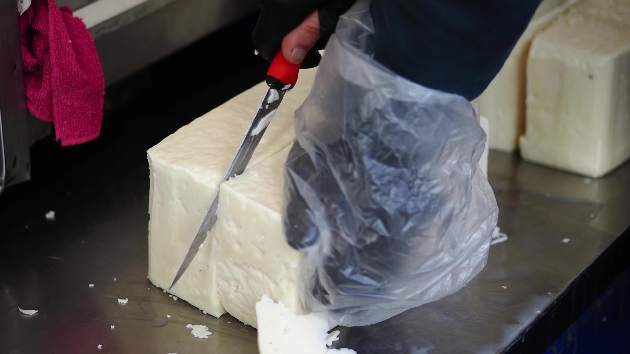 Close-up of Hand Slicing a Block of White Cheese