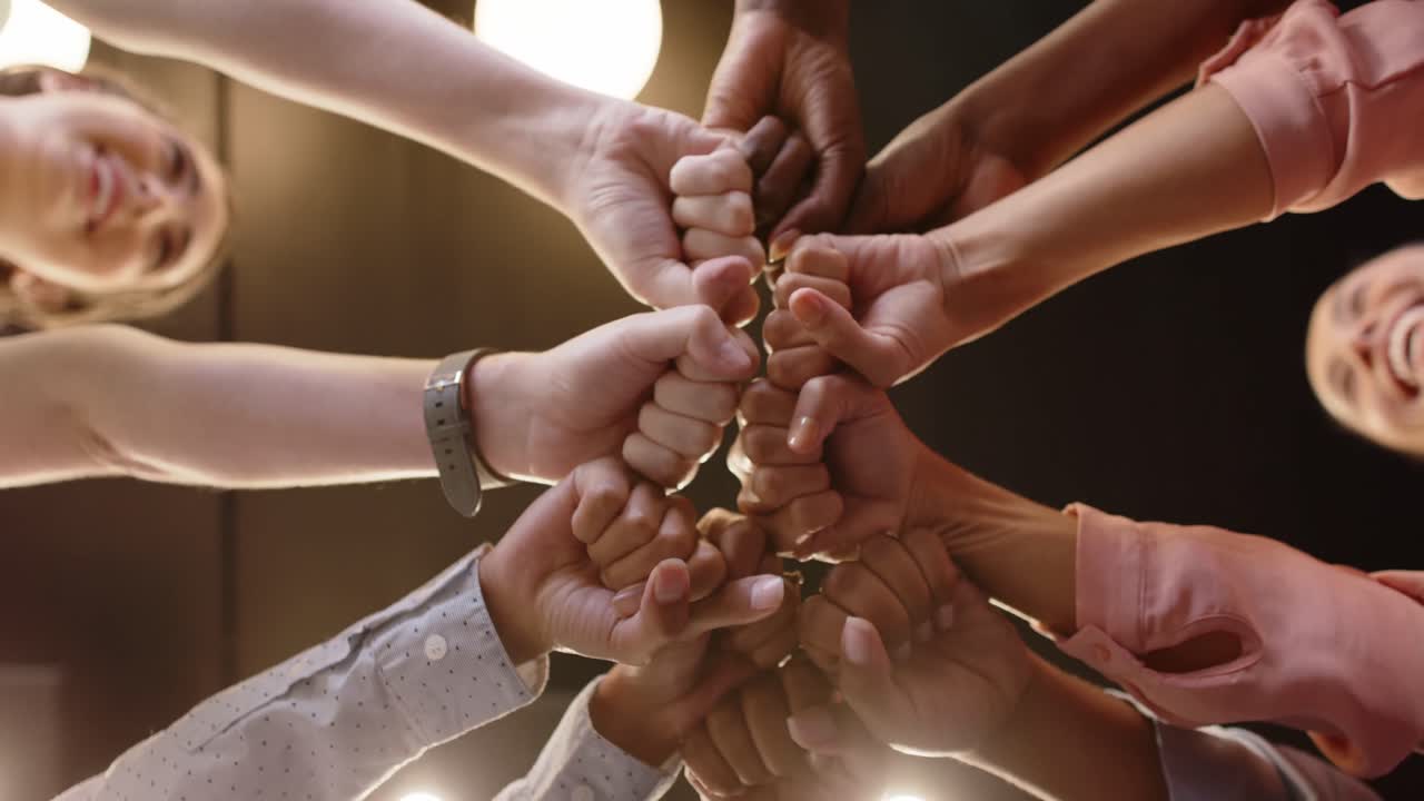 Low angle of group of happy diverse businesswomen bumping fists at office, in slow motion