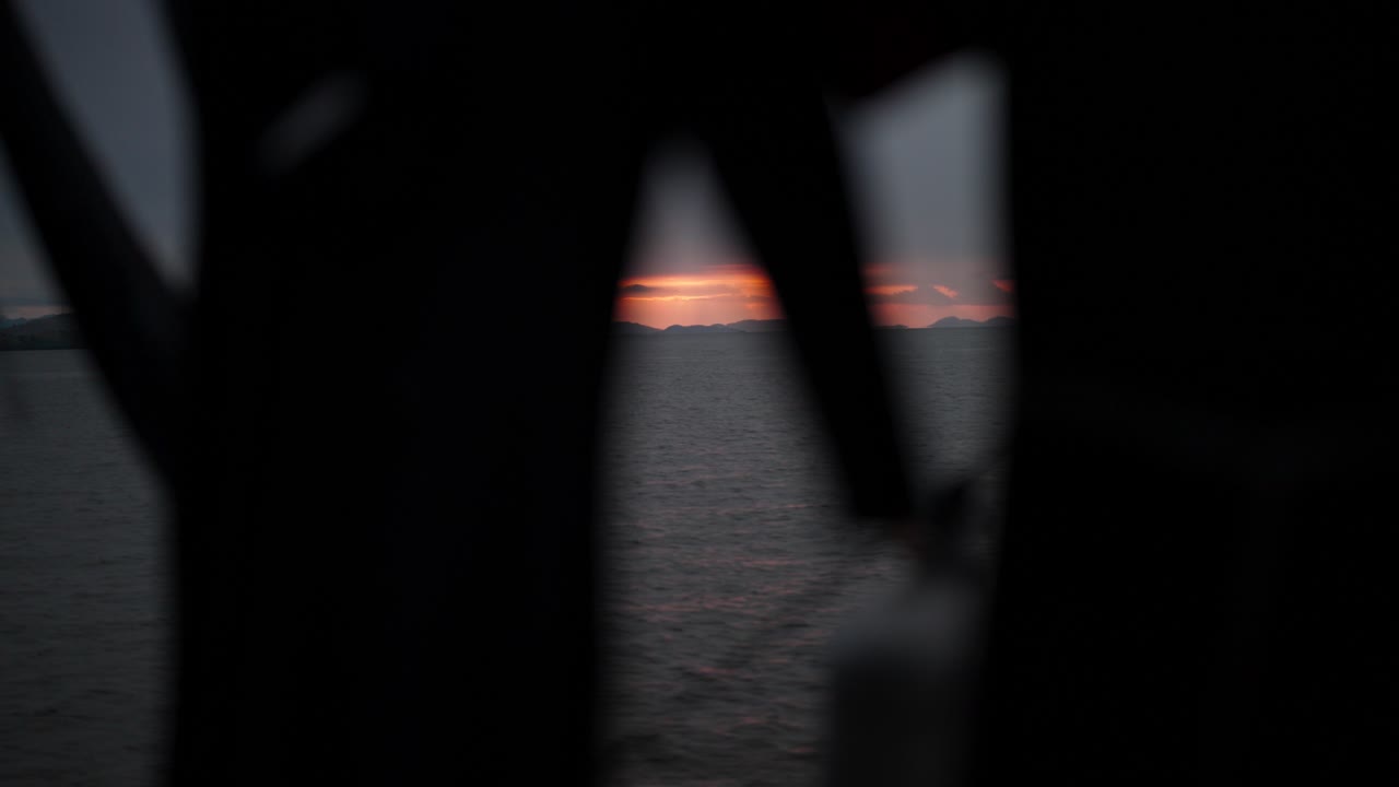 Primo piano di mute da sub in silhouette che sventolano al vento su una barca da immersione, con un tramonto sereno visibile sullo sfondo