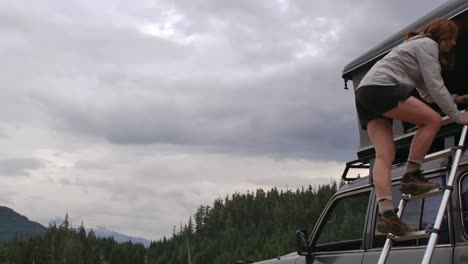 girl climbs in land cruiser's rooftop tent at lakeside in forest slomo