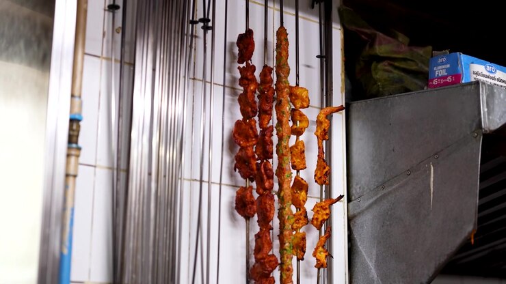 Primo piano di spiedini di carne speziata appesi in una cucina professionale con una luminosa illuminazione interna