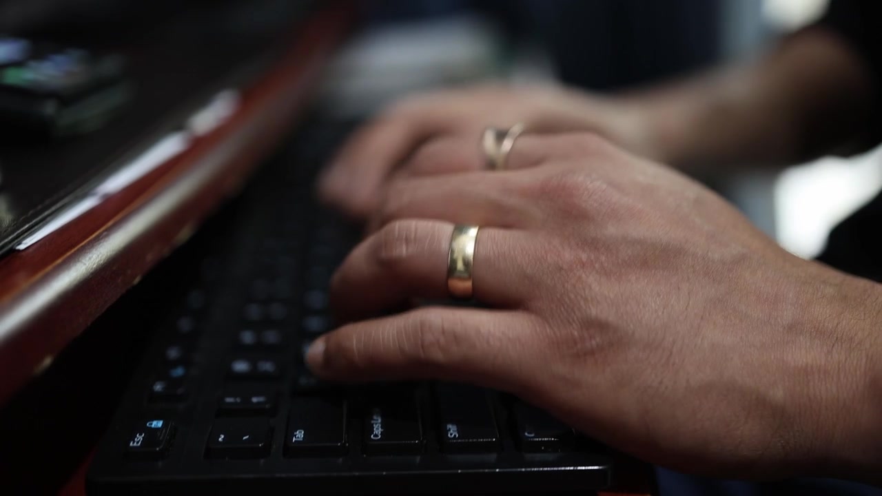 Detailed view of hands typing on a keyboard in a low-light setting. The composition captures the texture and focus of the fingers in motion, highlighting the dynamic energy of digital work.