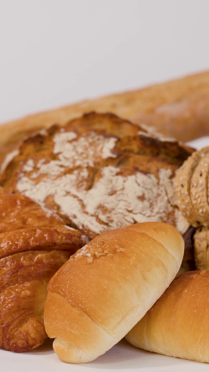 Close-up shot of hands arranging various fresh breads, croissants, and baguettes on white surface.