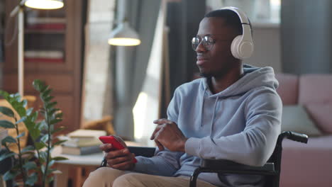 man using smartphone in a wheelchair while wearing headphones