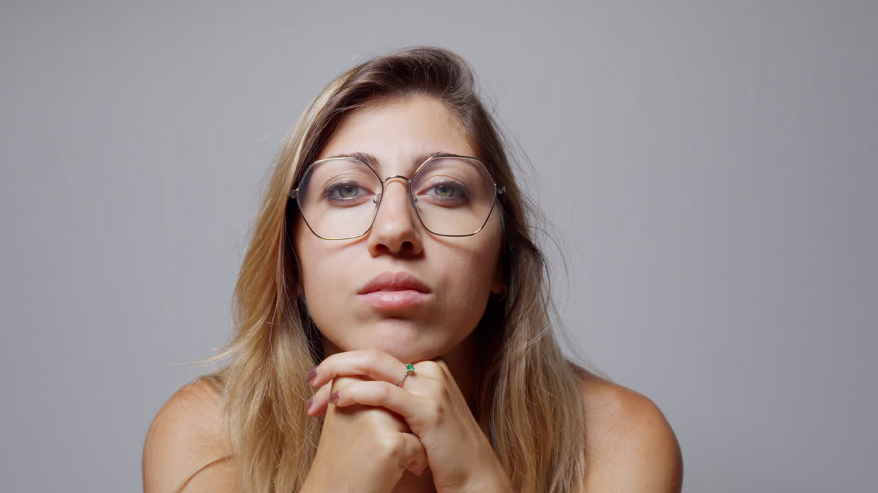 Close-up of a woman with long blond hair wearing glasses and nail polish. She rests her face on her hands, closes her eyes, and turns her gaze to the right