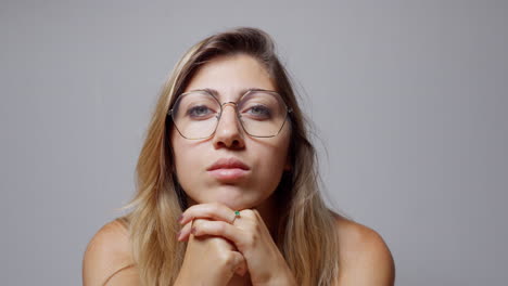 close-up of a woman with long blond hair wearing glasses and nail polish. she rests her face on her hands, closes her eyes, and turns her gaze to the right