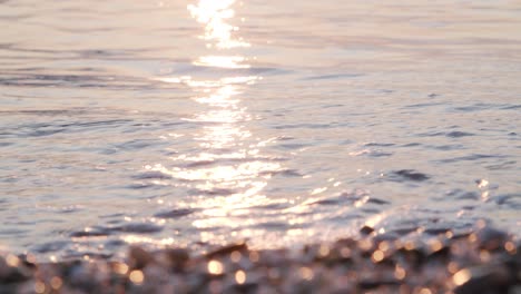 Close-up-calm-waves-ripple-on-sand,-defocused-pebbles-foreground,-Almeria,-Spain